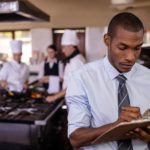 Male manager with tie writing on a clipboard in commercial kitchen