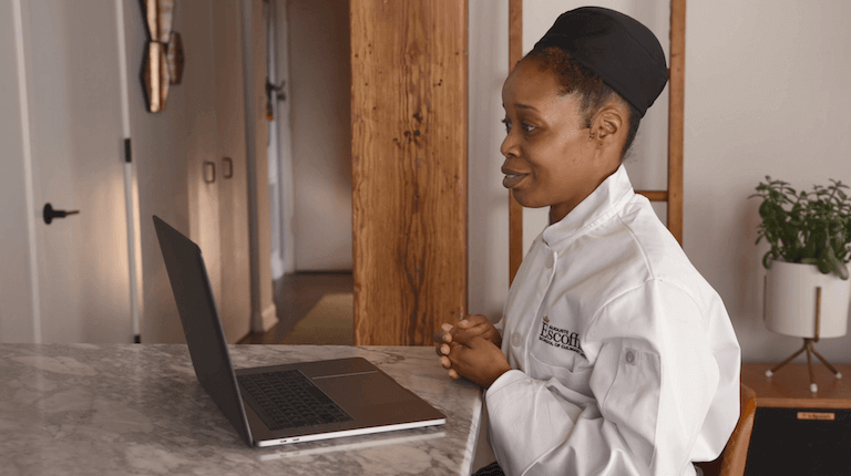 Online culinary student sitting at counter looking at laptop