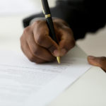 Person signing paper document with a black and gold pen