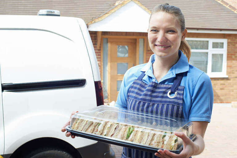 Smiling Caterer Delivering Tray Of Sandwiches To House