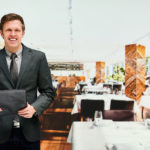 Smiling restaurant manager in a black suit holding a menu