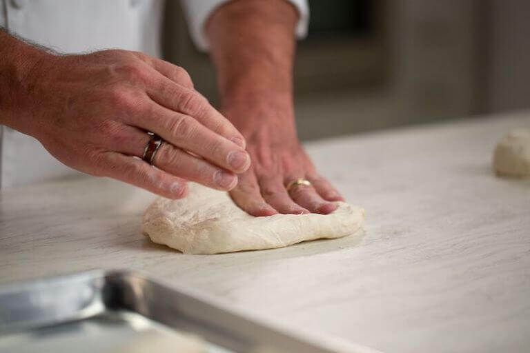 Chef kneading dough with their hands on a white counter