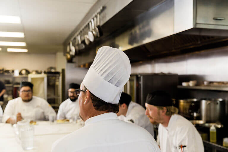 Chef talking to group of cooks and culinary students in a kitchen