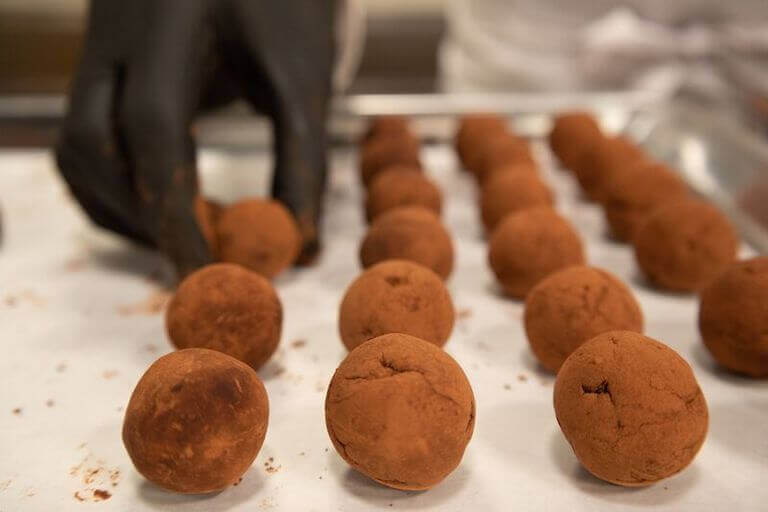 Chef with black gloves on placing chocolate truffles on a baking sheet