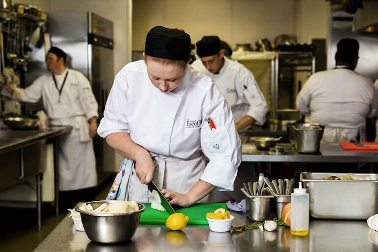 Escoffier student chopping an onion on a cutting board in the kitchen