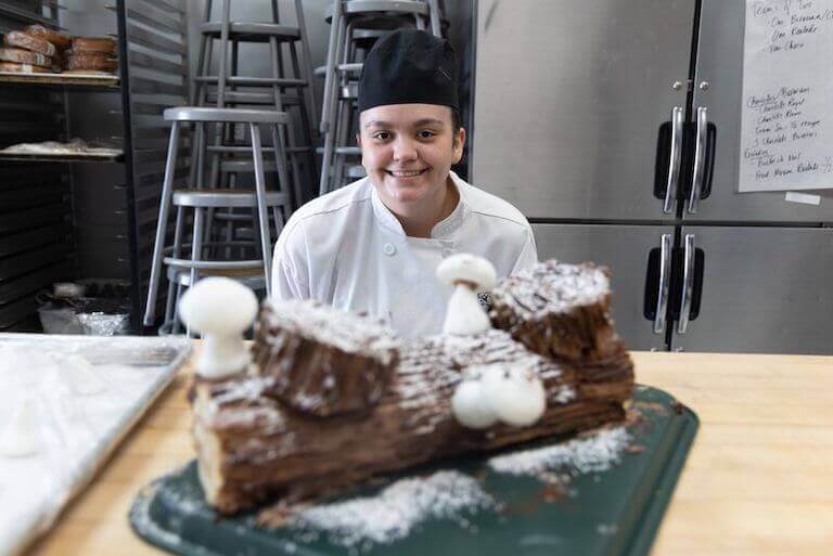 Escoffier student posing next to a cake that looks like a piece of wood