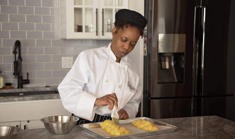 Online Escoffier student brushes butter on dough in her kitchen