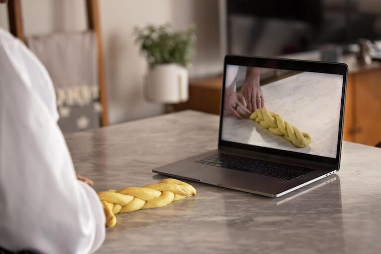 Laptop sitting on kitchen island with screen showing hands demonstrating how to wrap dough.