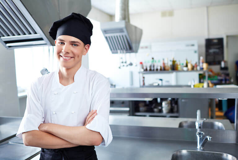 Smiling chef wearing black toque hat in kitchen