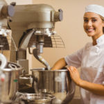 Smiling woman in bakery using dough kneading machine