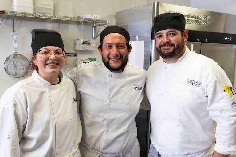 Three Escoffier students standing together and smiling in a kitchen