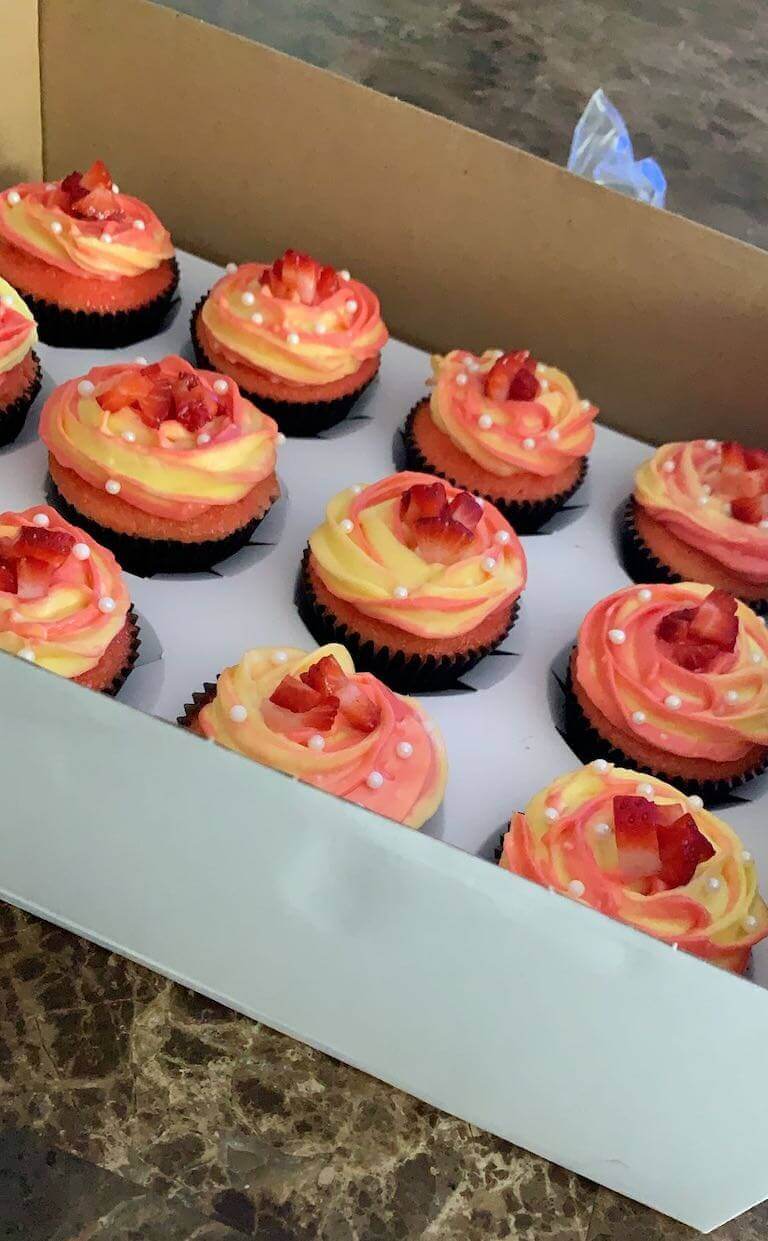 A white box of chocolate cupcakes with red and yellow floral frosting.