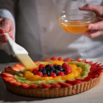 Brushing apricot glaze on a fruit pie with strawberrries, kiwis