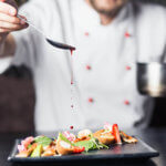 Chef using spoon to pour red sauce over a plate
