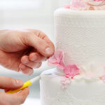 Pastry chef using scalpel to shape pink flower on white cake
