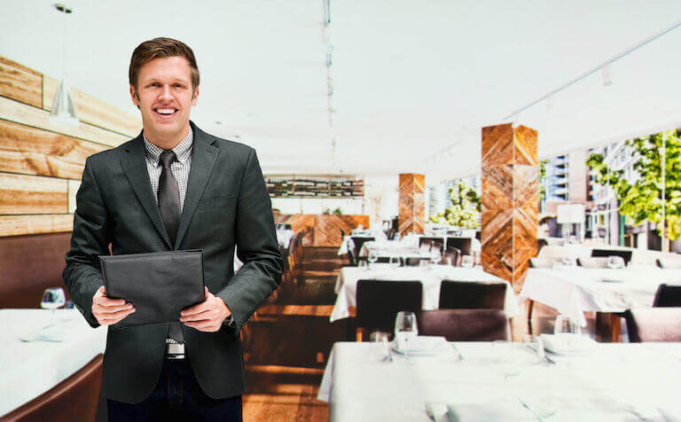 Smiling restaurant manager in a black suit holding a menu