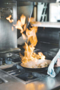 A Chef is holding a pan with a flame in it while coking