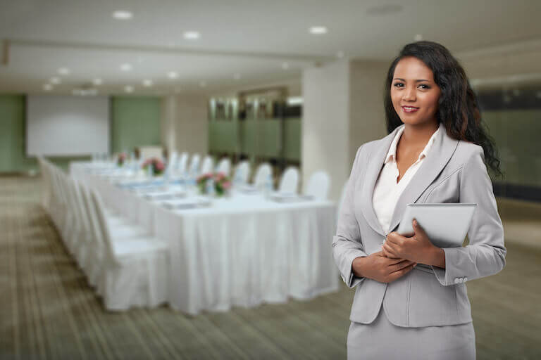 Hotel manager stands in a banquet hall holding a tablet