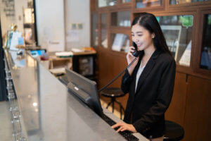 Hotel receptionist smiles while talking on the phone and looking at the computer at the front desk