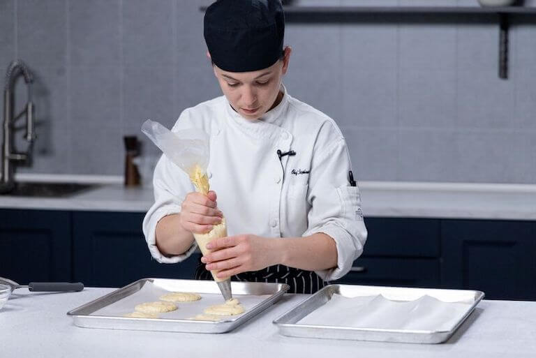 Pastry chef using a piping bag to make Baked Alaska on a baking sheet