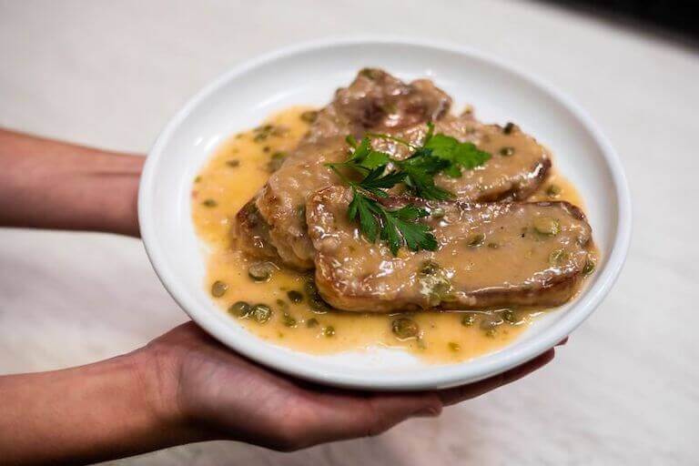 Two hands holding Seitan Piccata on a white dish
