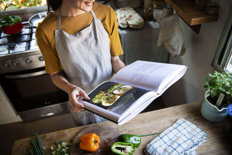 woman with apron reading a cookbook in the kitchen