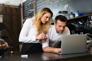Cafe manager and waitress take notes as they look at a laptop
