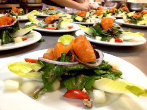 Multiple plates of salad topped with salmon sit on the counter in a kitchen
