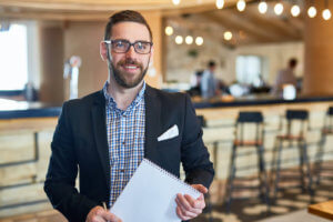 Restaurant manager stands in front of the bar holding a notebook