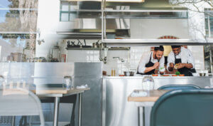 Two Chefs are leaning over a counter as they plate dishes