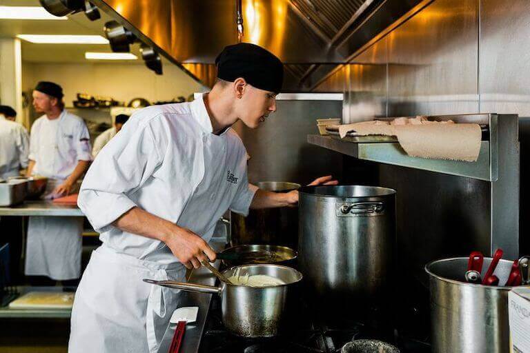 Escoffier student checking a pot in a professional kitchen