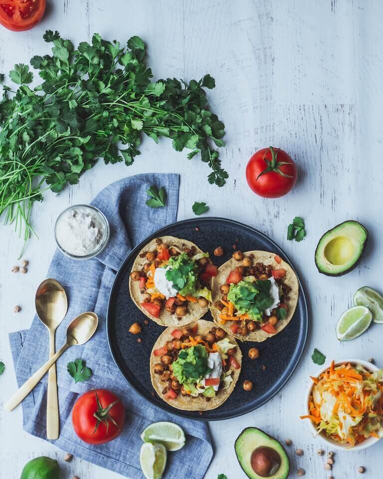 Plant-based tacos with sour cream and avocado sit on a black plate