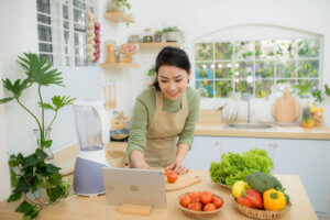 Female online student cutting a tomato in her kitchen while she looks at her laptop