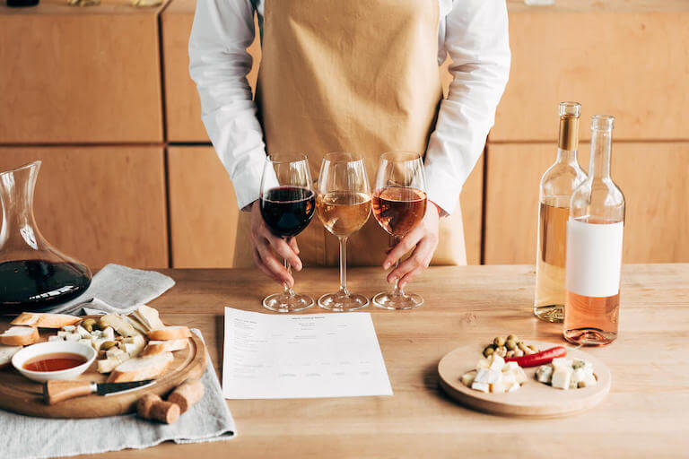 sommelier in an apron holding 3 glasses of wine on a wooden table