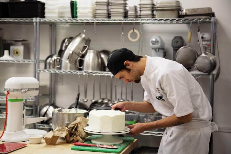 A Pastry Chef is icing a cake in an industrial kitchen