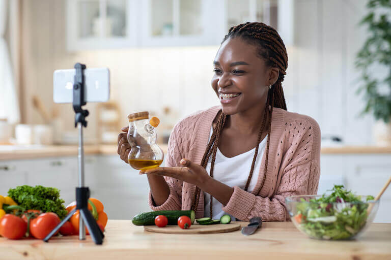A nutrition coach is filming a video on her phone with cucumber, tomatoes, and other vegetables