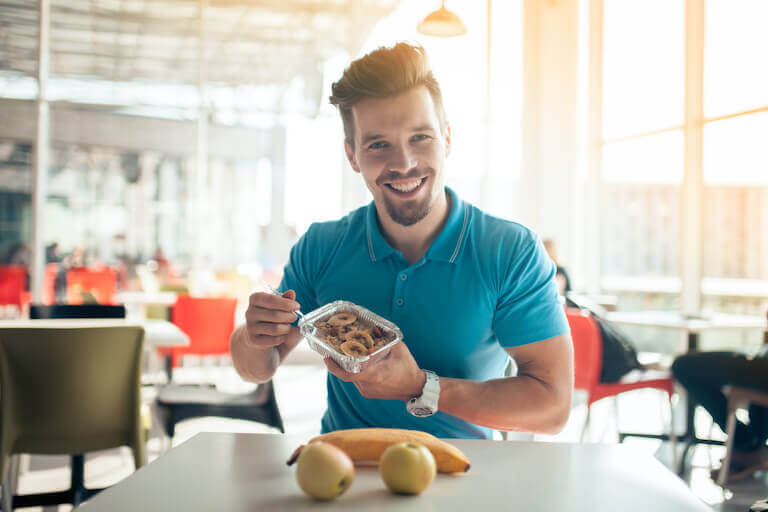 A young adult is eating a healthy breakfest with bananas and apples in a cafe