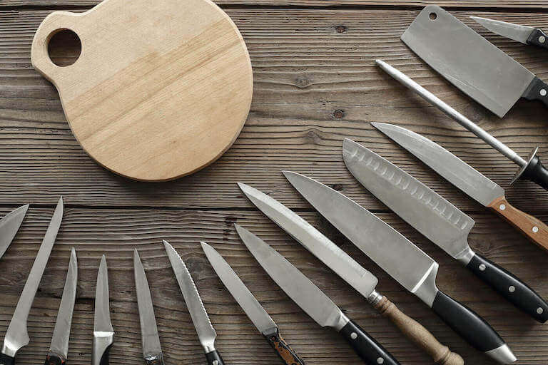 An assortment of kitchen knives around a cutting board 