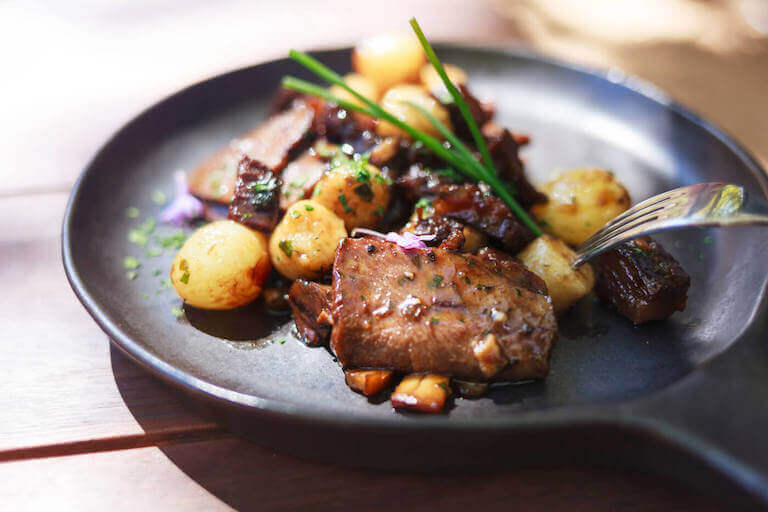 Beef and potatoes dish on a black plate pan