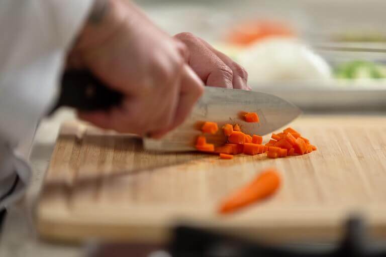 Chef cutting carrots on a wooden cutting board
