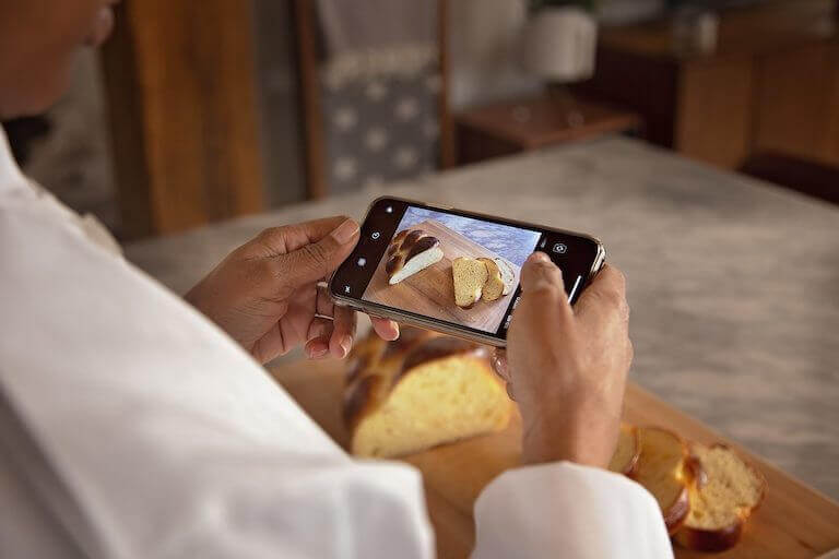 Culinary student taking a picture on phone of sliced bread on a wooden board