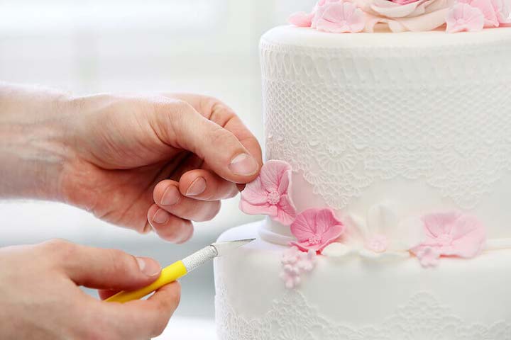 Pastry chef using scalpel to shape pink flower on white cake