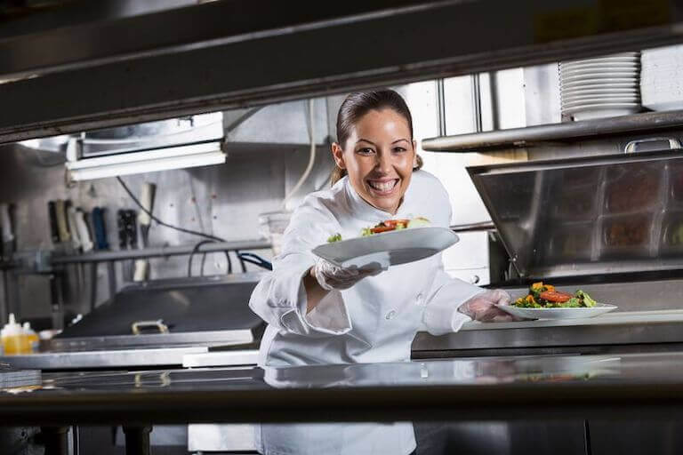 Smiling chef holding two white plates with salad in a kitchen