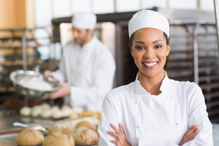 Smiling female chef in a bakery with loaves of bread
