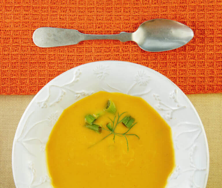 A bowl of squash soup with garnishes and a spoon