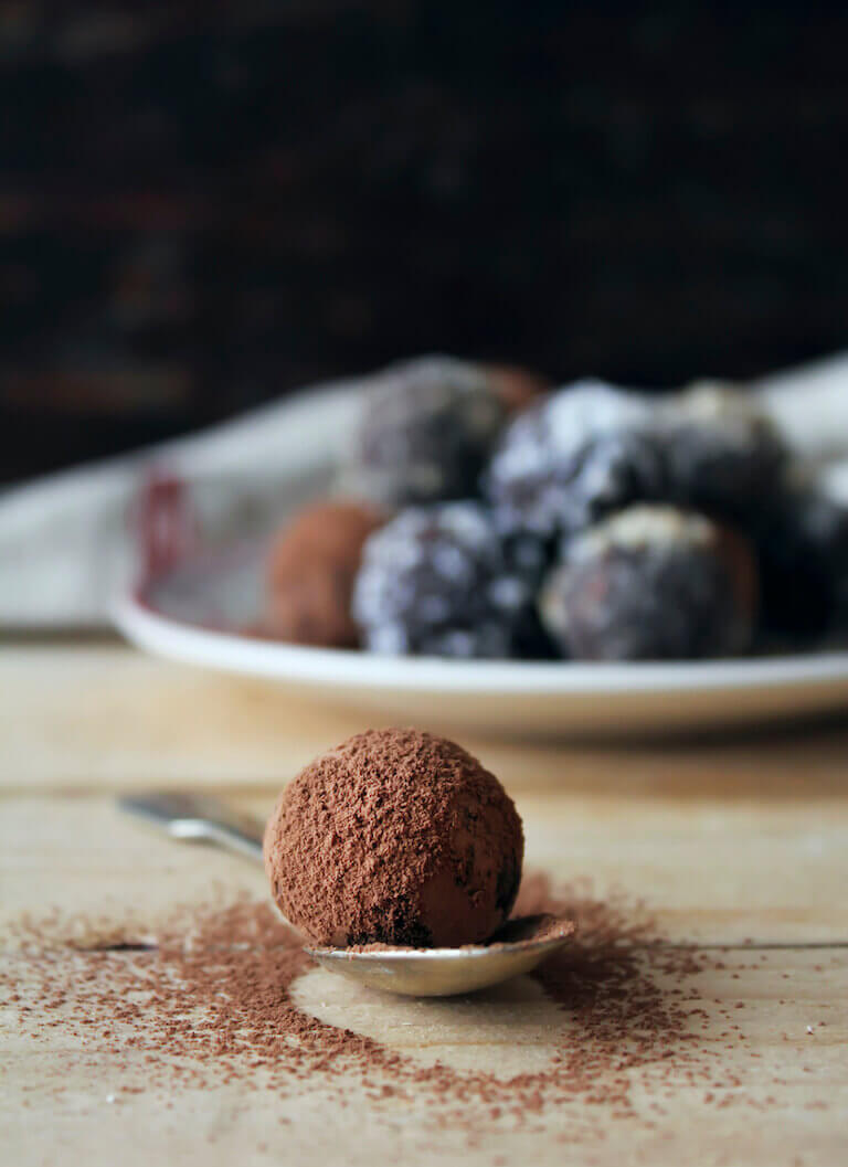 A chocolate truffle sits on a spoon with chocolate powder sprinkled on the table