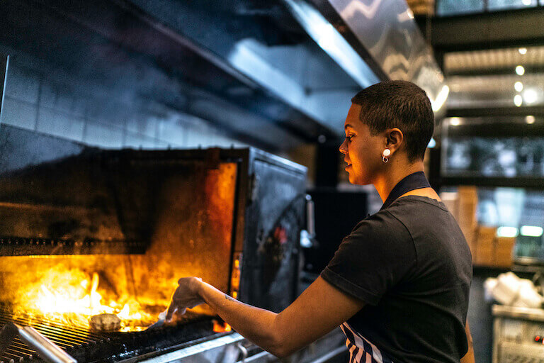 Chef flipping a burger on a grill with flames