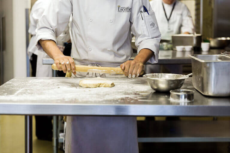 Escoffier pastry chef rolling flour dough in kitchen