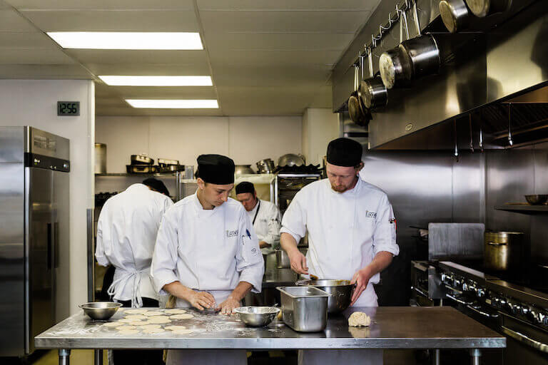 Escoffier students kneading dough flour in kitchen