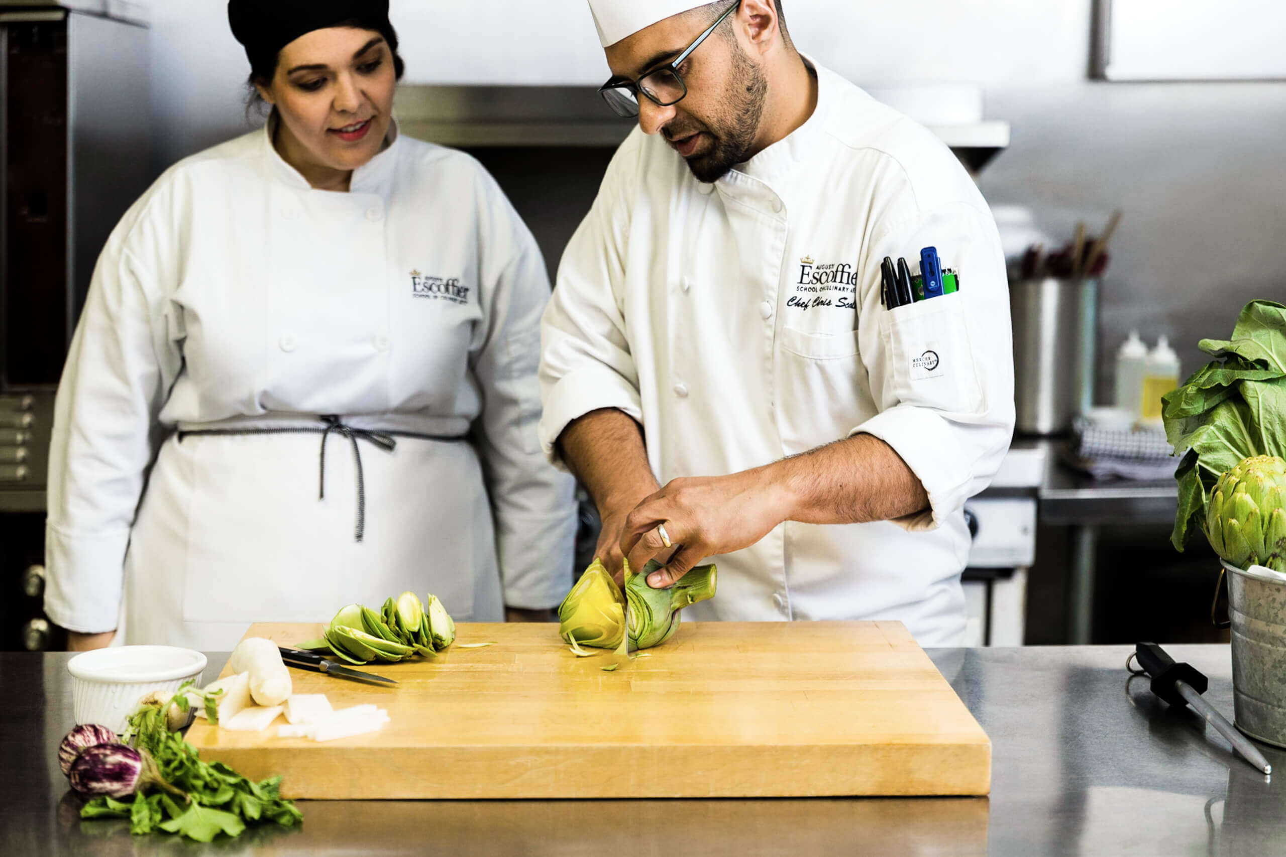 Male chef instructor showing female culinary student how to chop vegetables